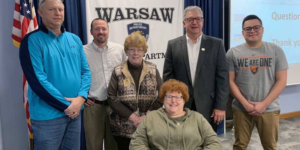 Kosciusko Leadership Academy group photo of six adults in front of a Warsaw Police Department banner.