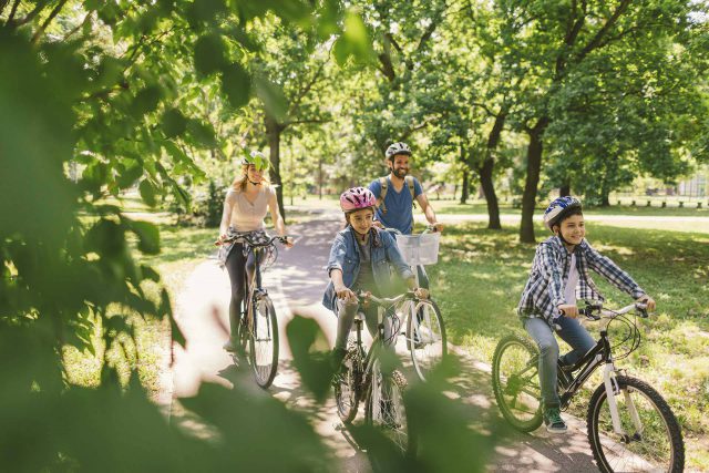 Two adults and two children riding bicycles while wearing helmets on the Winona Lake greenway.