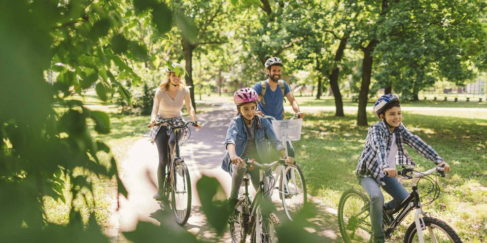 Two adults and two children riding bicycles while wearing helmets on the Winona Lake greenway.