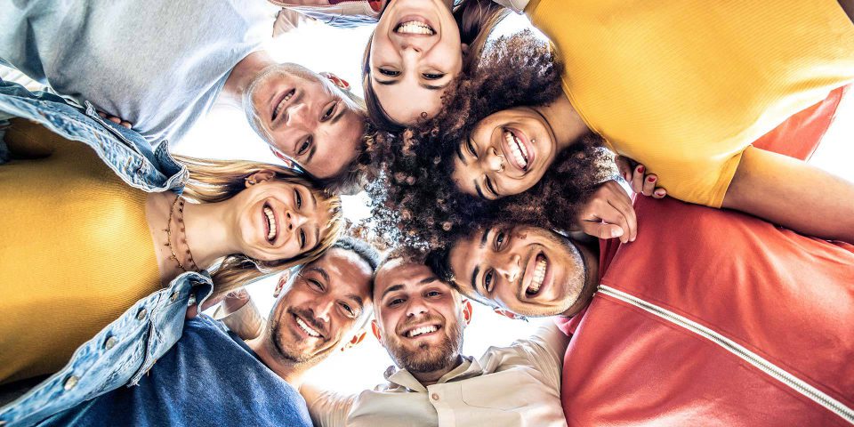 Group of 7 adults with arms around each other looking down at the camera